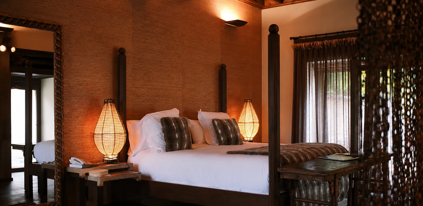 A bedroom at El Despenadero with a dark four-poster bed, grasscloth walls and woven lantern lamps