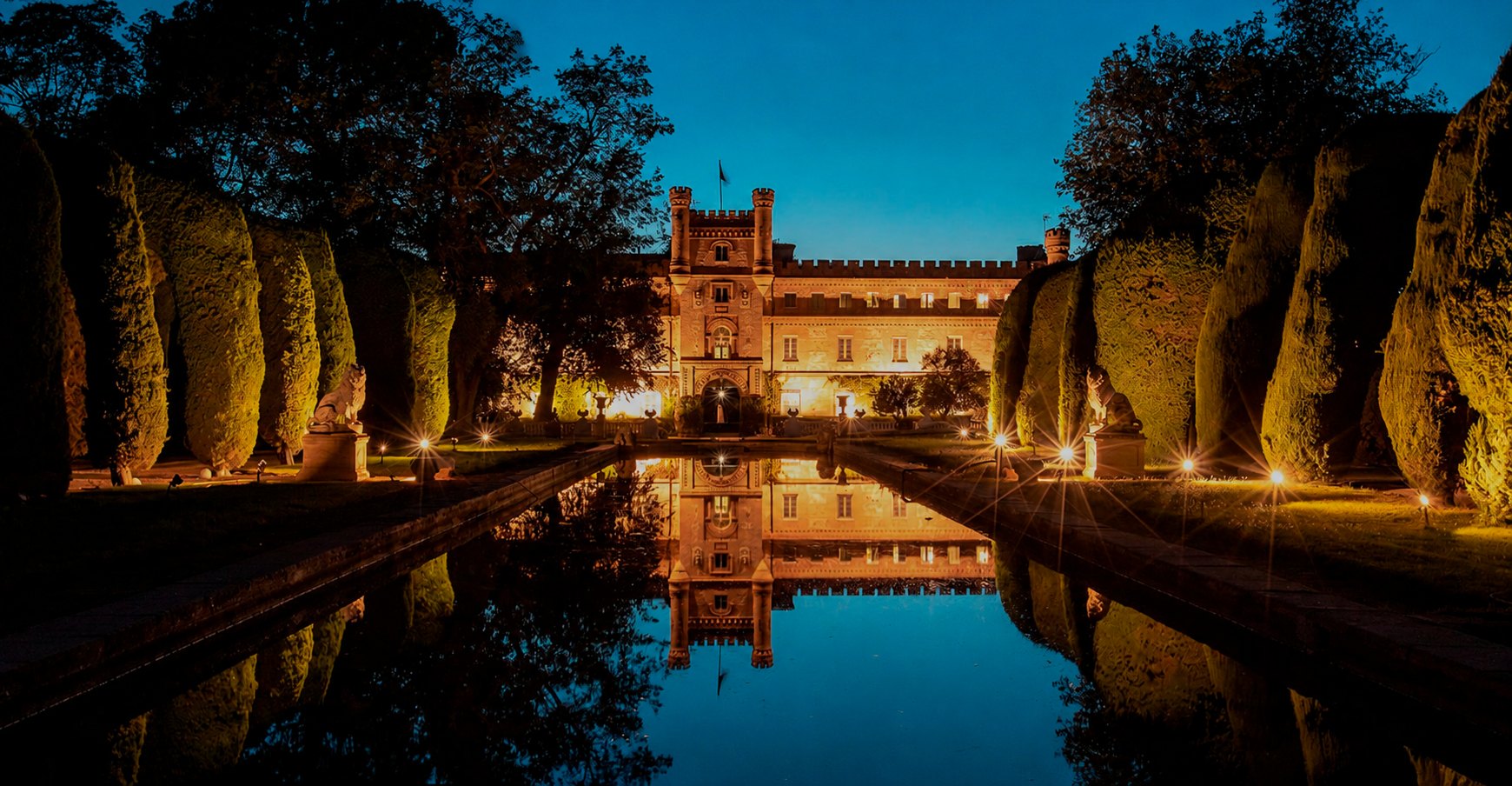 The floodlit house at Ventosilla mirrored in the formal water canal at dusk, clipped cypresses either side